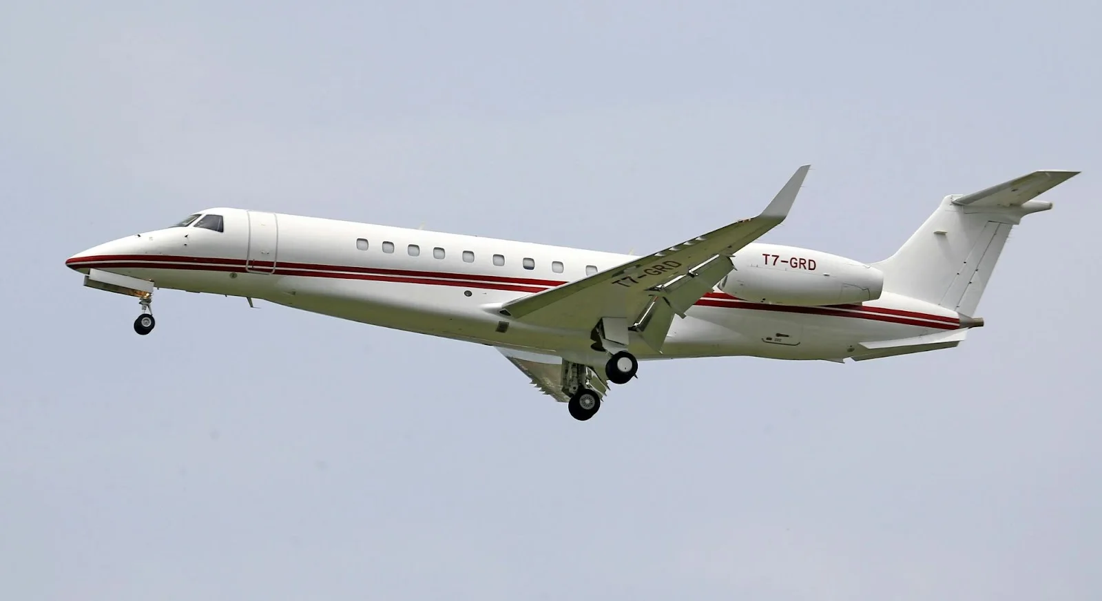 White private jet with red accent stripes flying through cloudy skies, showcasing luxury aircraft for empty leg flights