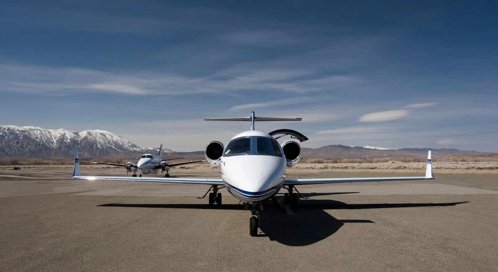 White private jet positioned on remote airstrip with snow-capped mountains, showcasing empty leg charter opportunities
