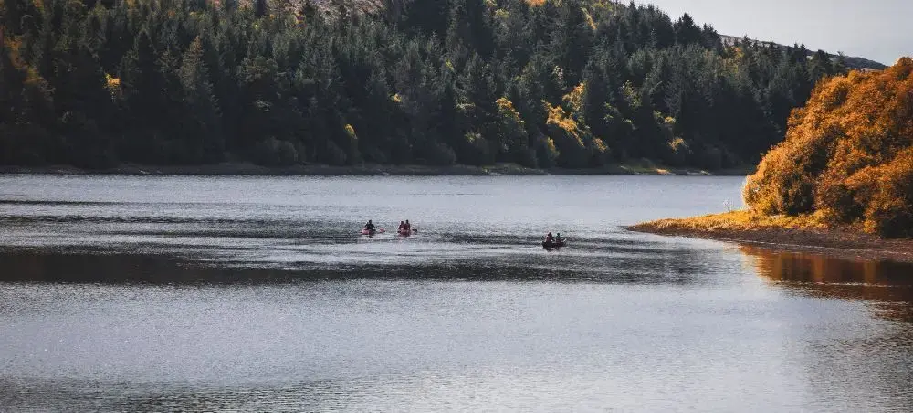 Kayakers paddling on a tranquil lake surrounded by autumn forest in Bannau Brycheiniog, Wales
