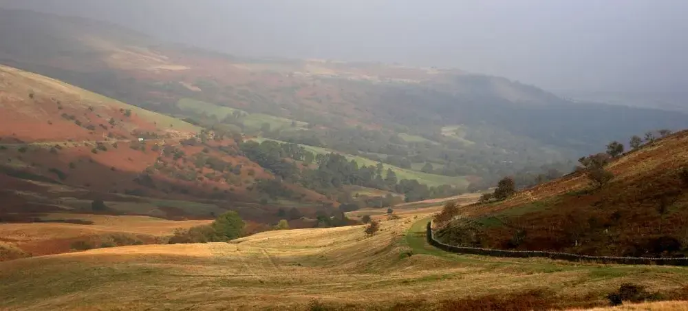 Sweeping autumn valley in Bannau Brycheiniog National Park, with golden moorland, dry stone walls and mist-covered hills
