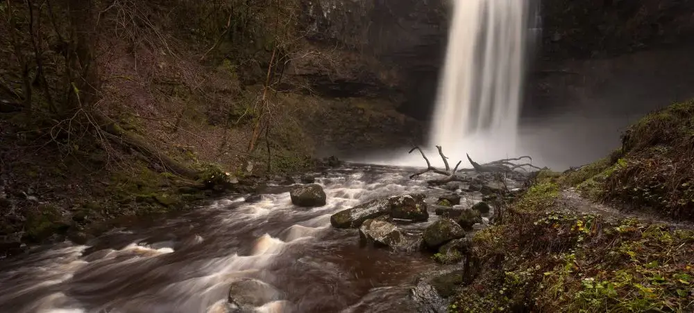 Dramatic waterfall cascading into a rocky river gorge in Bannau Brycheiniog, a breathtaking natural landmark accessible via private jet charter to South Wales