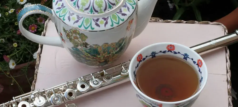 Ornate floral teapot, matching teacup with fresh tea, and a silver flute arranged on a garden table in Bath, England