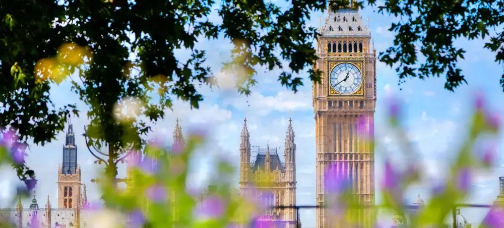 Big Ben and the Houses of Parliament framed by trees and flowers, iconic landmarks for private jet charter visitors to London