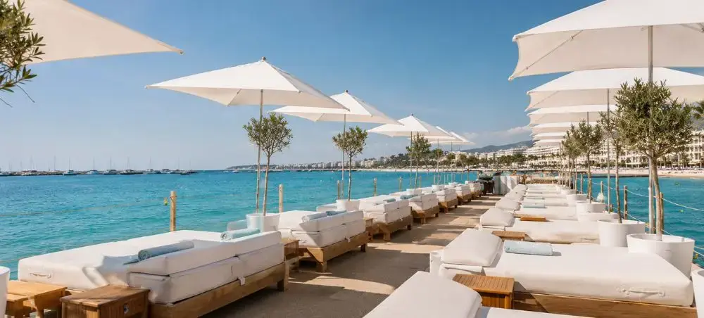 Luxury beach club on the Cannes Croisette with white sun loungers, umbrellas, and turquoise Mediterranean views