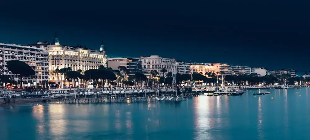 Cannes waterfront at night with the iconic Carlton Hotel illuminated along the Croisette, reflecting on the calm French Riveria waters