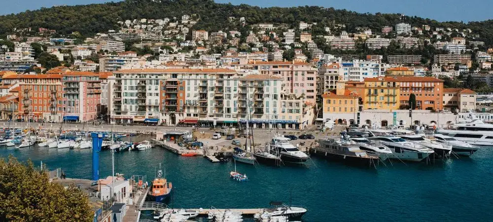 Luxury yachts moored in the vibrant harbour of Cannes, France, with colourful Mediterranean waterfront buildings and lush hillside villas in the background