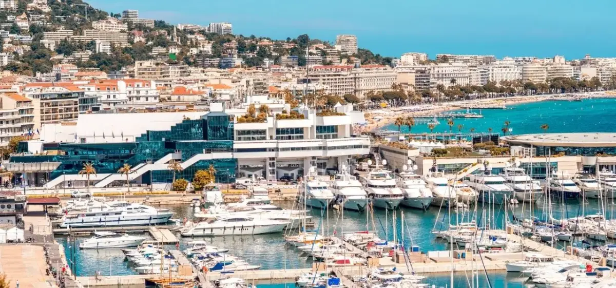 Cannes harbour lined with luxury superyachts and the Palais des Festivals, with the iconic Croisette beachfront and hillside villas stretching along the French Riviera coastline