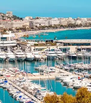 Cannes harbour lined with luxury superyachts and the Palais des Festivals, with the iconic Croisette beachfront and hillside villas stretching along the French Riviera coastline