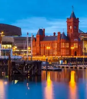 Cardiff Bay at dusk featuring the Pierhead Building and Senedd, reflecting warm golden lights across the waterfront marina