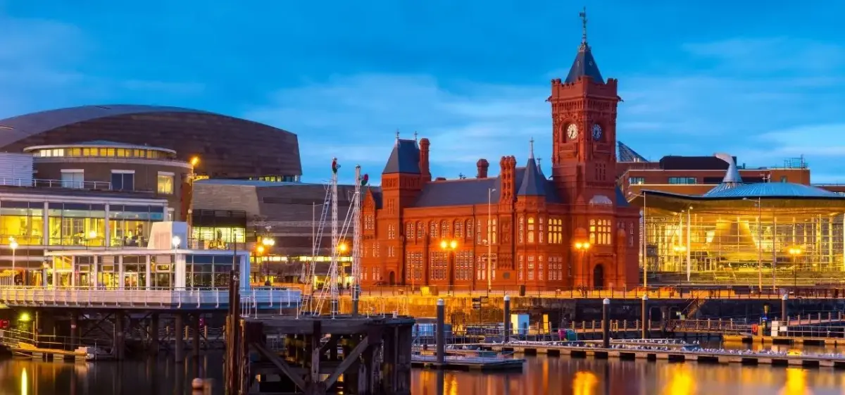 Cardiff Bay at dusk featuring the Pierhead Building and Senedd, reflecting warm golden lights across the waterfront marina