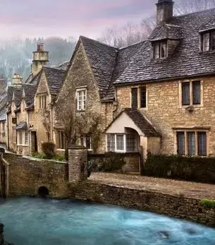 Honey-stone cottages lining a tranquil stream in the Cotswolds, England, a destination reachable by private jet charter