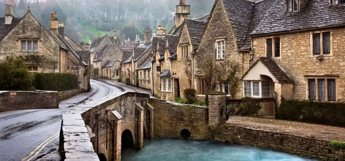 Honey-stone cottages lining a tranquil stream in the Cotswolds, England, a destination reachable by private jet charter