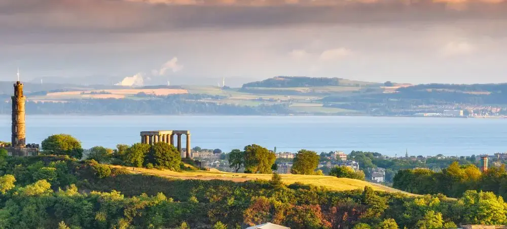 Panoramic view of Edinburgh's Calton Hill with Nelson Monument and National Monument overlooking the Firth of Forth at sunset