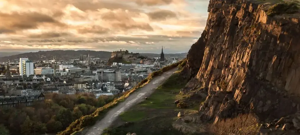 Panoramic view of Edinburgh city skyline with Edinburgh Castle on the hill under a dramatic golden sunset sky