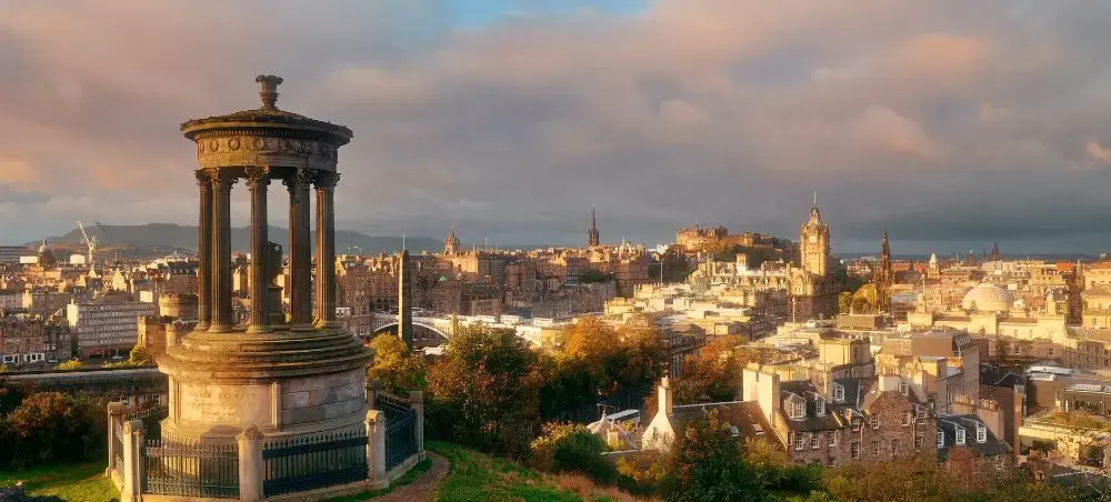 Panoramic golden-hour view of Edinburgh's skyline from Calton Hill, with the Dugald Stewart Monument and Edinburgh Castle