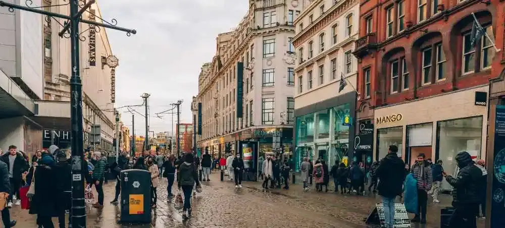 Bustling pedestrian shopping street in England with historic architecture, stores and crowds of shoppers on cobblestones