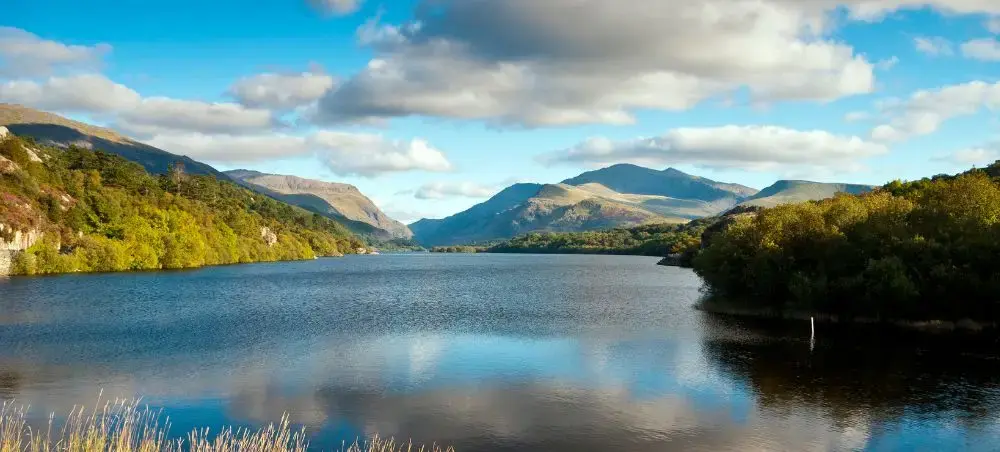 Tranquil lake in Eryri (Snowdonia) reflecting mountain peaks and blue sky, a destination accessible by private jet charter