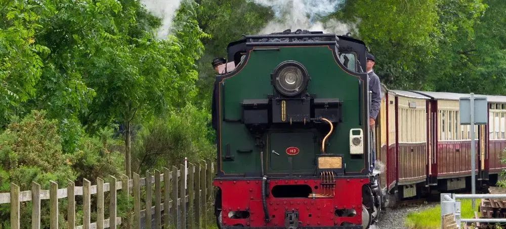 Historic steam train travelling through lush green Eryri countryside, a scenic way to explore Snowdonia's landscapes