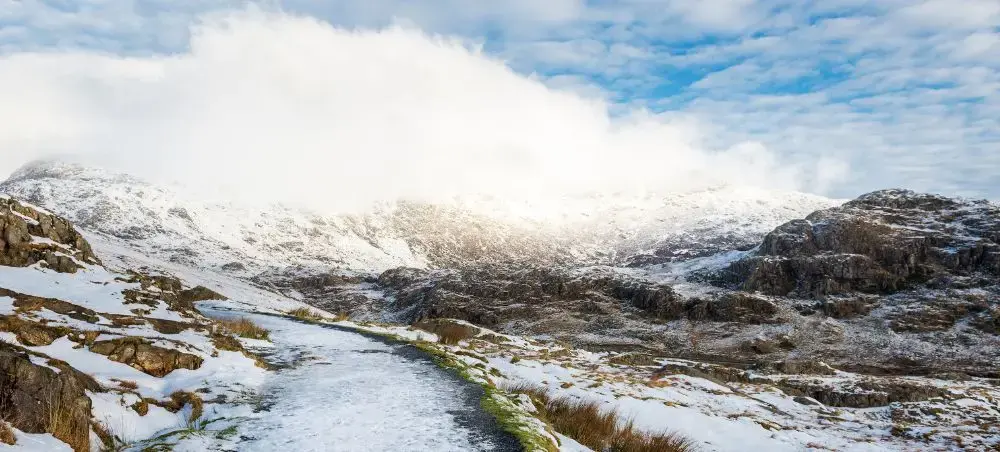 Snow-dusted mountain path winding through the rugged peaks of Eryri, Snowdonia, under a dramatic winter sky in North Wales