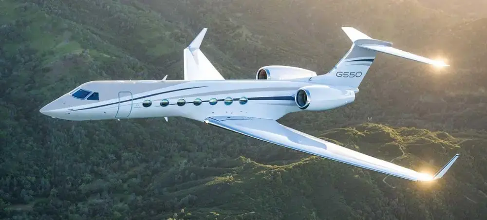 Gulfstream G550 private jet in flight over lush green hills, representing luxury charter travel to Wales with Jetbay
