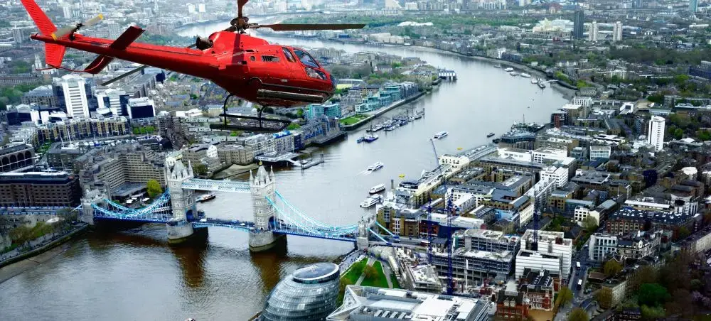 Red helicopter flying over Tower Bridge and the River Thames on a private charter flight above central London