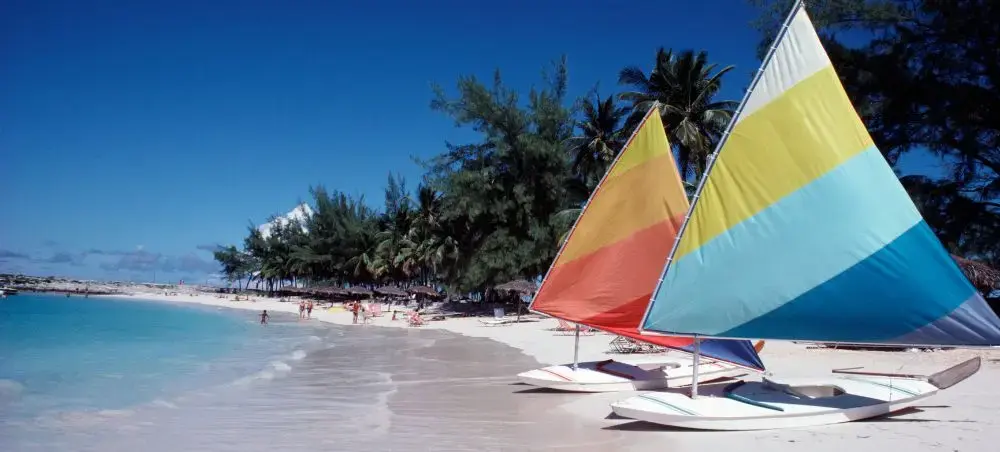 Colourful sailboats on a pristine white sand beach in Barbados, with waters and palm trees lining the shore near Holetown