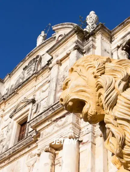 Golden lion sculpture adorning the ornate baroque facade of León Cathedral in Nicaragua under a vivid blue sky