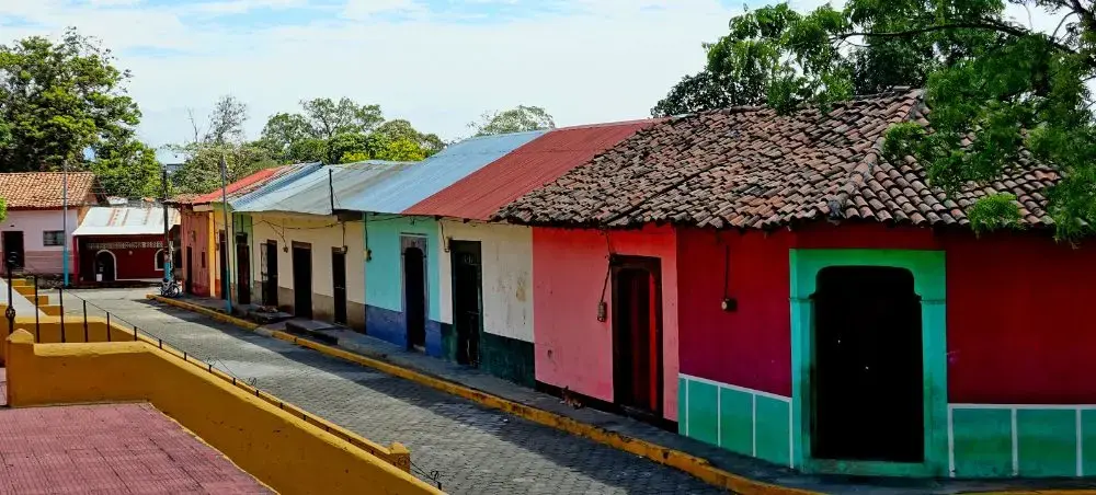 Colourful colonial street in León, Nicaragua, with vibrant red, pink and teal facades lining a cobblestone road under a bright sky