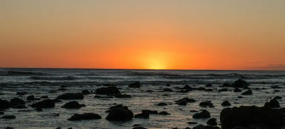 Golden sunset over the Pacific Ocean coast near León, Nicaragua, with waves rolling over volcanic rocks along the shoreline