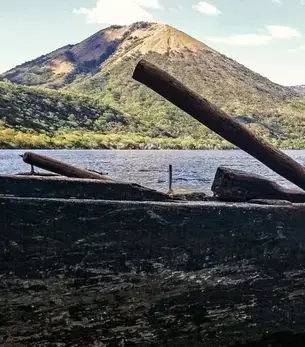 Rustic wooden boat on Lake Xolotlán with twin volcanic peaks of León, Nicaragua rising in the background under a clear sky