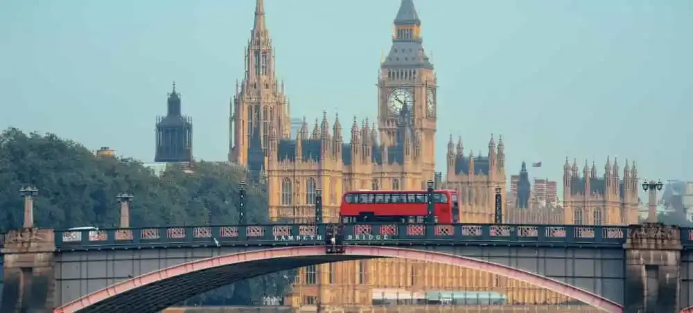 Red double-decker bus crossing Lambeth Bridge with the Houses of Parliament and Big Ben in the background; London landmarks