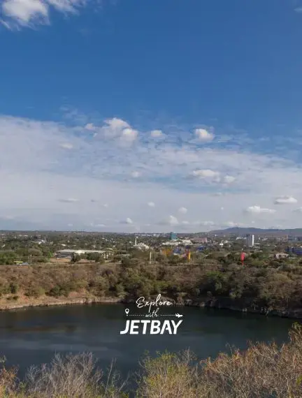 Panoramic view of Managua cityscape from Tiscapa Lagoon Natural Reserve, with volcanic crater lake in the foreground and the city skyline stretching toward distant mountains