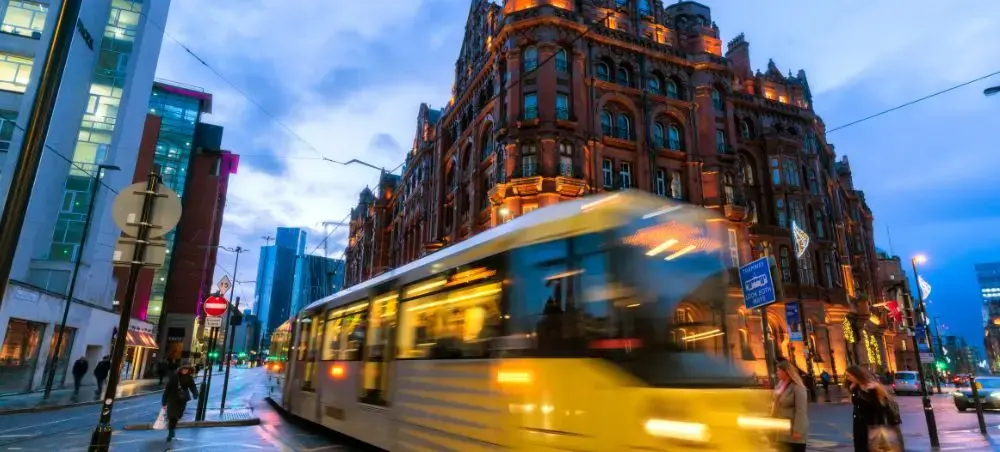 Manchester city centre at dusk with the Metrolink tram passing the iconic red-brick Midland Hotel
