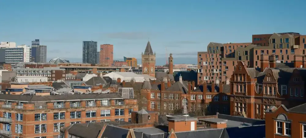 Manchester city skyline featuring Victorian red-brick buildings and modern high-rises under a clear blue sky