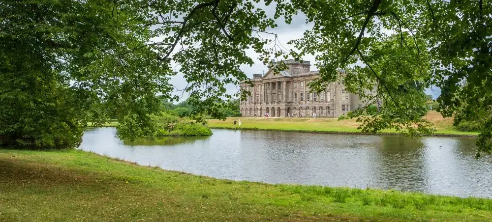 English country estate with facade reflected across a lake, surrounded by parkland near Cheshire and Manchester, England