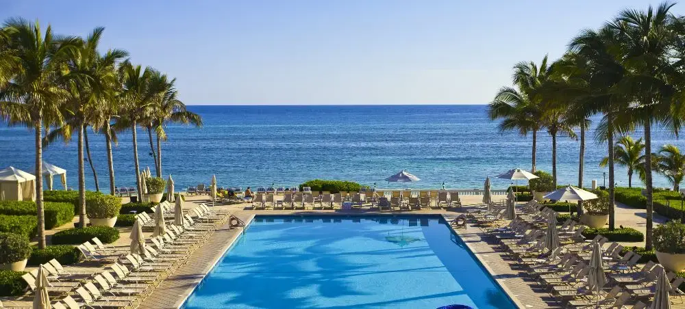 Luxury beachfront resort pool in Montego Bay, Jamaica, with lounge chairs, palm trees, and turquoise Caribbean sea views