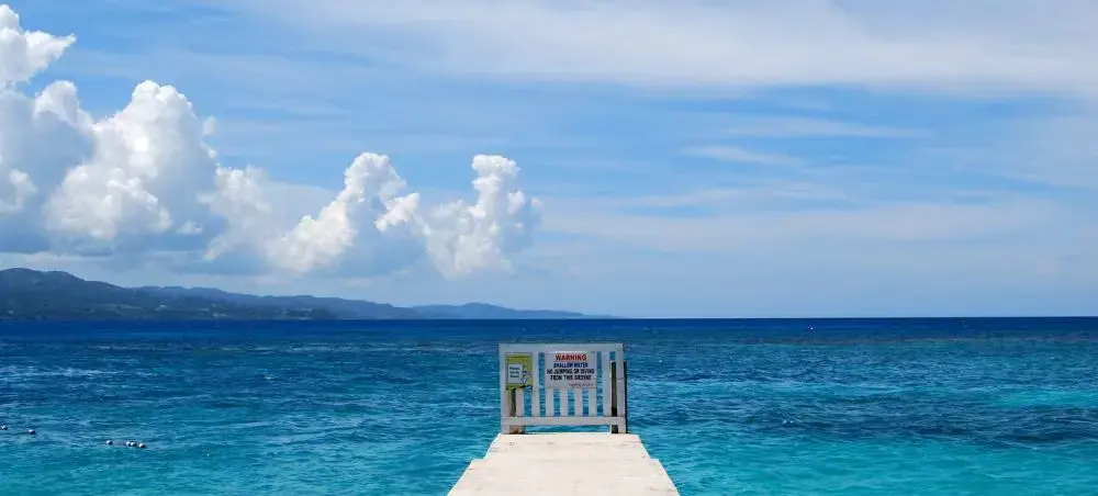 Scenic ocean pier overlooking the crystal-clear turquoise waters of Montego Bay, Jamaica, with lush green mountains on the horizon