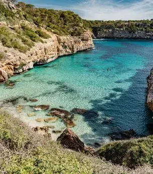 Secluded turquoise cove with dramatic limestone cliffs and pine-covered hillsides near Palma, a premier private jet destination in Mallorca, Spain