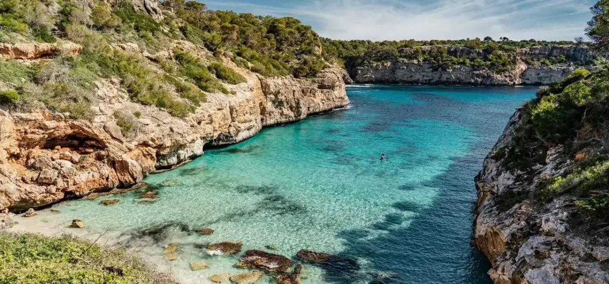 Secluded turquoise cove with dramatic limestone cliffs and pine-covered hillsides near Palma, a premier private jet destination in Mallorca, Spain