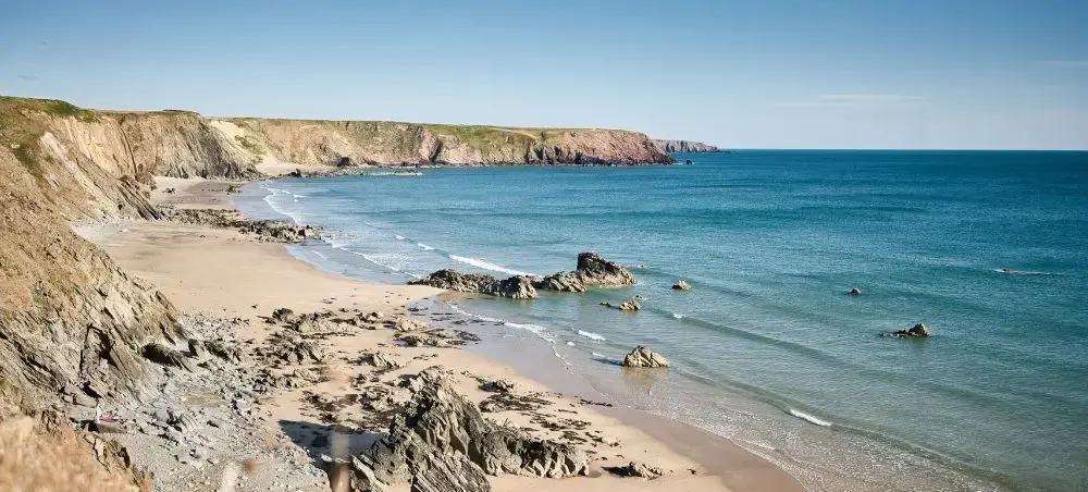 Secluded sandy cove along the Pembrokeshire Coast, with rugged cliffs, rocky outcrops and turquoise waters