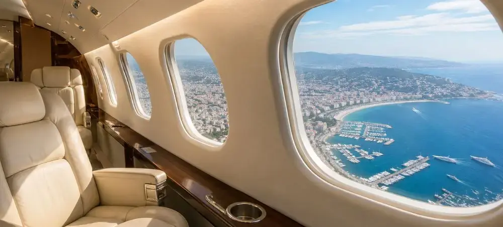 Luxury private jet cabin with cream leather seats overlooking Cannes coastline and marina on the French Riviera