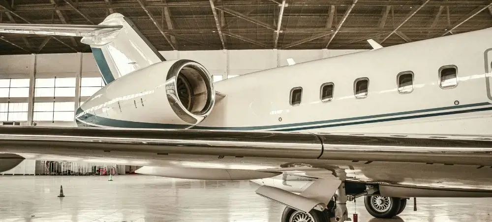 White private jet with teal accent stripe parked in aircraft hangar, showcasing the fuselage, engine, and landing gear available for charter to Linz-Land District