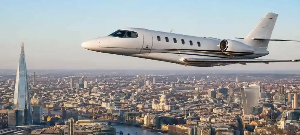Private jet flying over London skyline with The Shard and St Paul's Cathedral visible below, charter flight to England