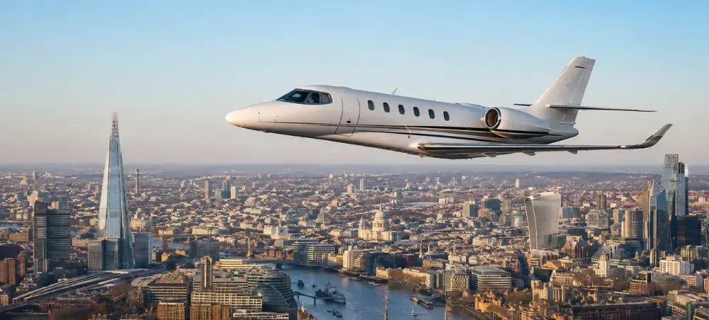 Private jet flying over the London skyline with the Shard and Thames River visible below on a clear day