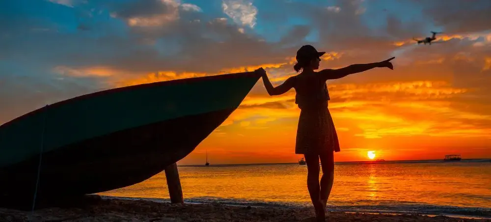 A young woman on the shores of Roatan, Honduras pointing at a private jet charter during sunset