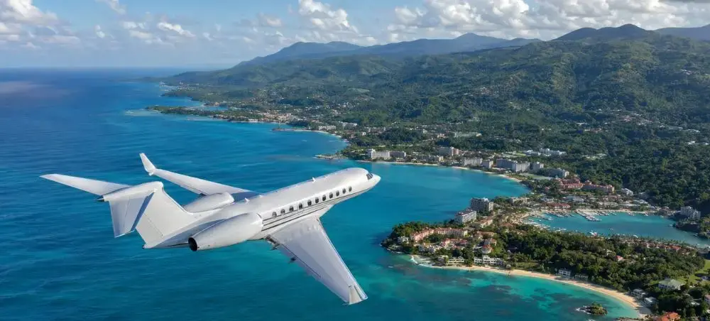 Private jet flying above Ocho Rios, Jamaica with coastline and green hills below