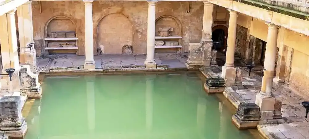 The ancient Roman Baths in Bath, England, featuring a green thermal pool surrounded by Roman columns and stone architecture