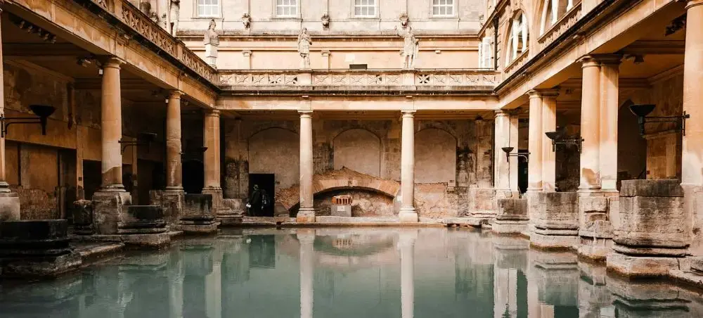 The ancient Roman Baths in Bath, England, featuring a thermal pool surrounded by stone columns and Georgian-era statues