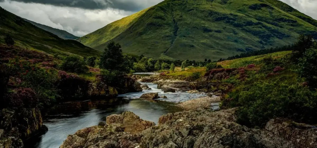 Rocky Highland river winding through a remote Scottish glen with heather-covered slopes, accessible by private jet charter