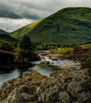 Rocky Highland river winding through a remote Scottish glen with heather-covered slopes, accessible by private jet charter